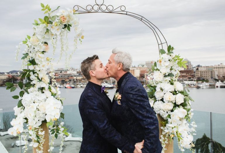 Grooms kissing under floral arch
