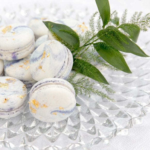 White and purple macaroons with gold flakes on a glass plate with green foliage