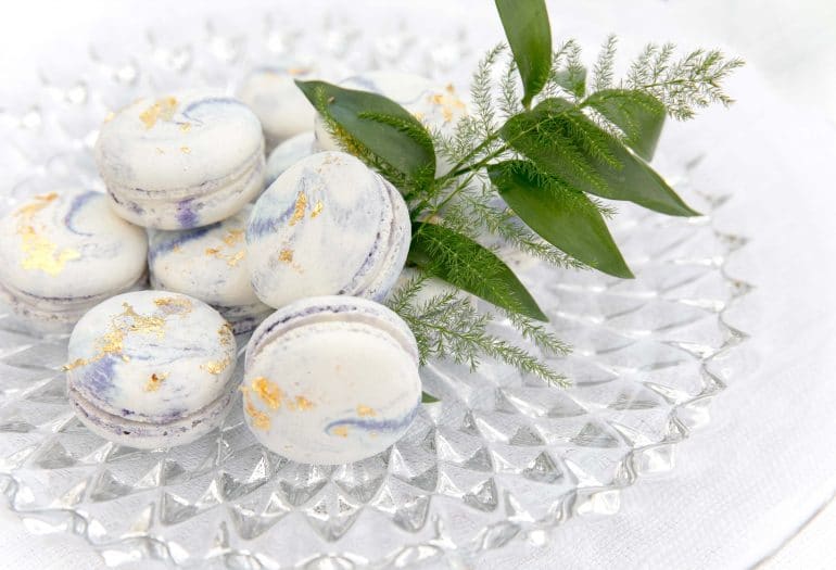 White and purple macaroons with gold flakes on a glass plate with green foliage