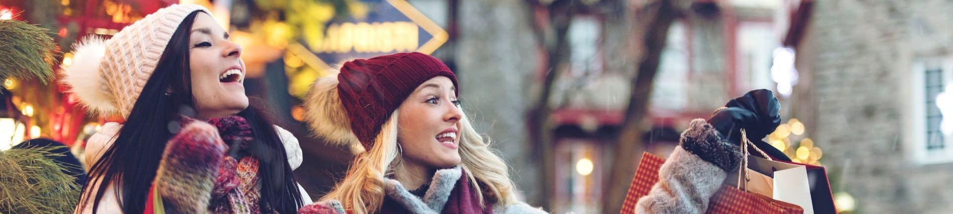 two women window shopping on street in winter with bags for holiday package