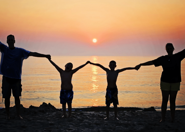 Silhouette of family of four holding hands on a beach at sunset