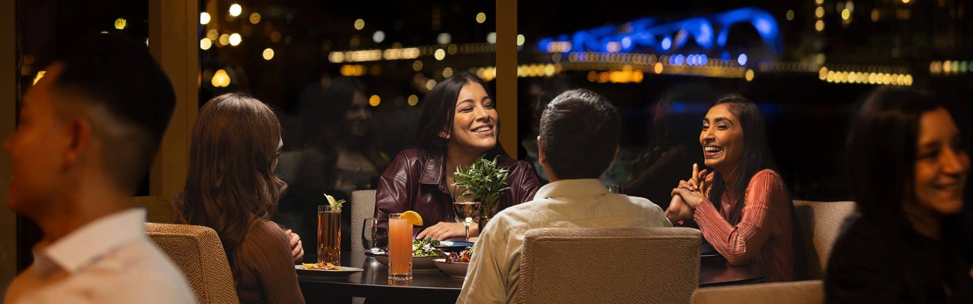 Table of four at table in Aura Restaurant, blue bridge in background, enjoying Dinner Tasting Menu Package
