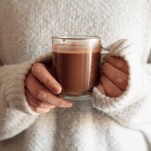 hot chocolate in a clear mug held by someone in white sweater