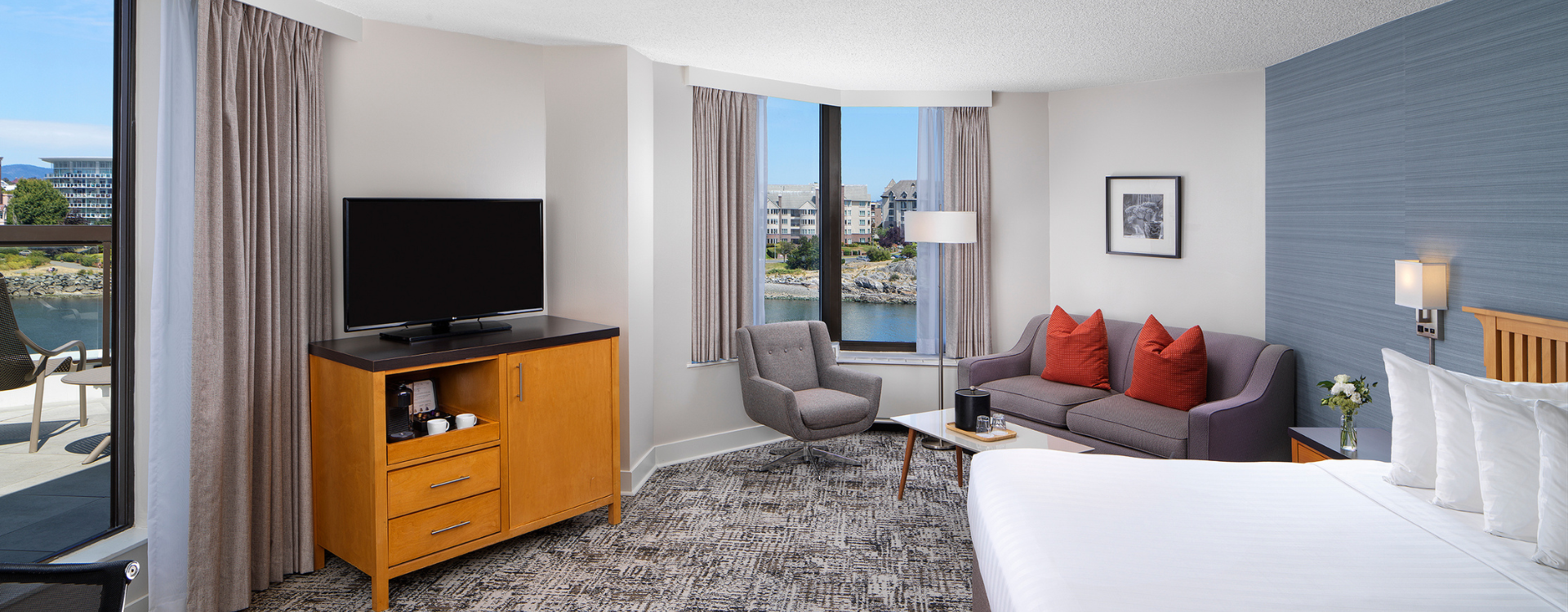 Laurel Wing Sunset Guestroom with king size bed, pull out sofa, armchair and tv in room, with a hint of the balcony and harbour views