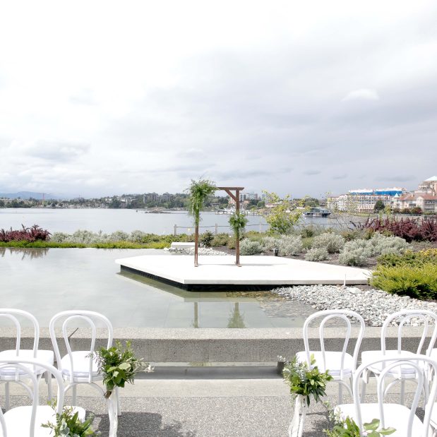 wedding ceremony set in the private gardens of Inn at Laurel Point, with white chairs facing a wedding arch in front of the outer harbour