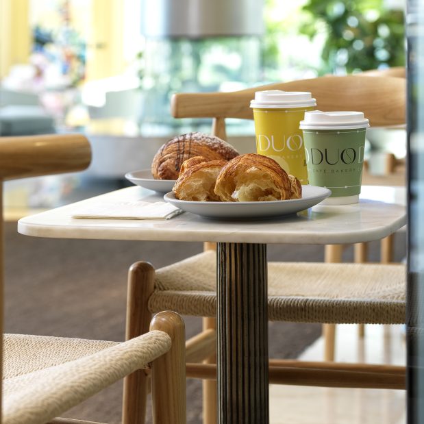 2 croissants (1 broken apart) and 2 to go cups from Duo Cafe Bakery on a table in the hallway outside Duo Cafe Bakery