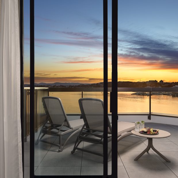 view of the sunset from the Laurel Wing sunset guestroom, 2 lounge chairs are seen from an open sliding door with a side table holding drinks and charcuterie on the balcony