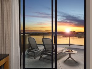view of the sunset from the Laurel Wing sunset guestroom, 2 lounge chairs are seen from an open sliding door with a side table holding drinks and charcuterie on the balcony