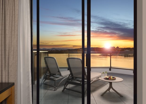 view of the sunset from the Laurel Wing sunset guestroom, 2 lounge chairs are seen from an open sliding door with a side table holding drinks and charcuterie on the balcony