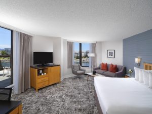 Laurel Wing Sunset Guestroom with king size bed, pull out sofa, armchair and tv in room, with a hint of the balcony and harbour views