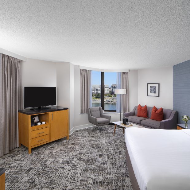 Laurel Wing Sunset Guestroom with king size bed, pull out sofa, armchair and tv in room, with a hint of the balcony and harbour views