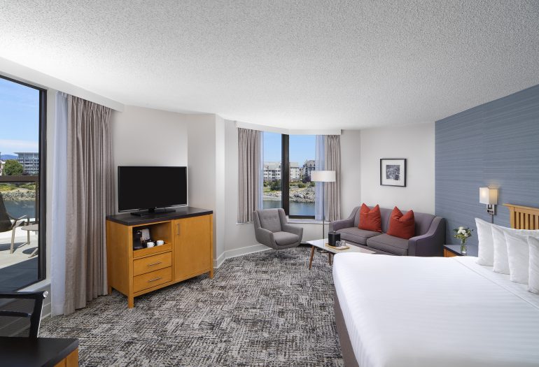 Laurel Wing Sunset Guestroom with king size bed, pull out sofa, armchair and tv in room, with a hint of the balcony and harbour views
