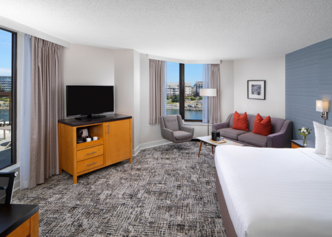 Laurel Wing Sunset Guestroom with king size bed, pull out sofa, armchair and tv in room, with a hint of the balcony and harbour views